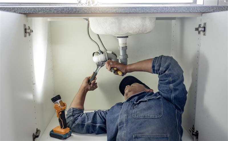 Plumber repairing pipes beneath a bathroom sink in Hacienda Heights